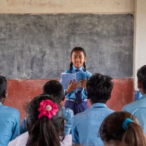 A pupil in front of a blackboard reading to her classmates